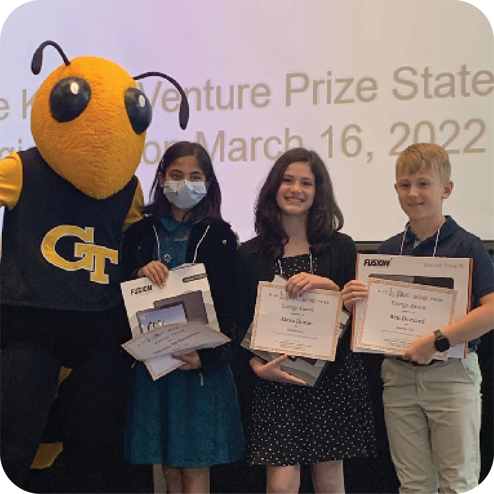Three smiling students holding prizes and standing next to Buzz (Georgia Tech's yellowjacket mascot).